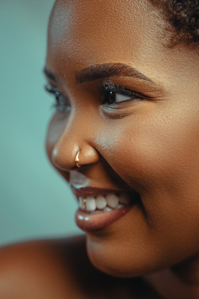 Candid studio portrait of a smiling woman with flawless skin and a nose ring.
